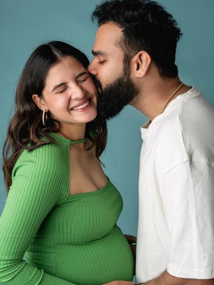 A fun and candid moment from a maternity shoot, with the partner giving a happy kiss on the cheek.