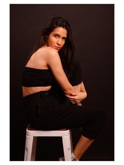 A minimalist and modern fashion portrait. The simple black outfit and dark background create a sleek and sophisticated look.