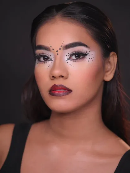 A graphic, tribal-inspired makeup look with bold black dots and white accents, showcasing precision and creativity.