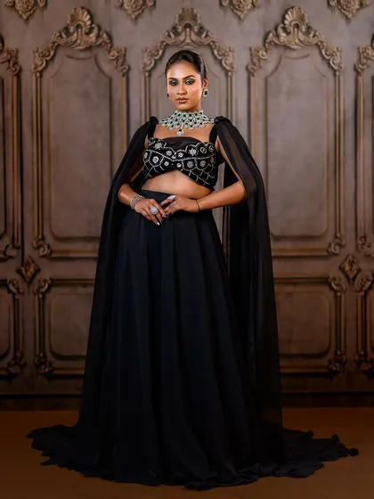 A powerful and elegant pose in a black lehenga with a cape. The ornate backdrop provides a beautiful contrast to the modern silhouette of the outfit.
