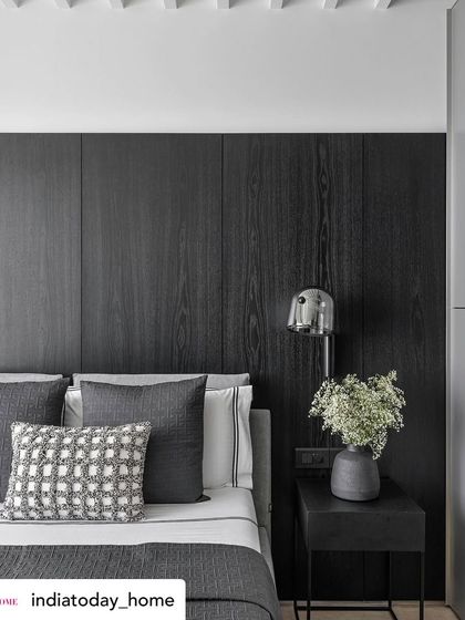 A close-up of a bedroom detail from a project featured in India Today Home. The dark wood paneling and textured grey bedding create a sophisticated, masculine feel, while the chrome bedside lamp adds a modern touch.