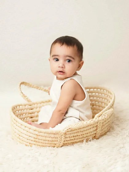 This little one is sitting in a simple wicker basket, looking back at the camera. Basket props are great for sitter sessions to keep the baby contained and happy.