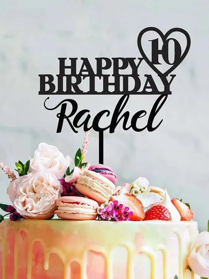 A "Happy Birthday Rachel" topper in black acrylic, shown on a beautiful cake with flowers and macarons, illustrating how a dark topper can create a striking contrast.