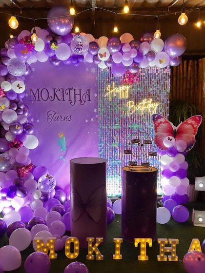 A rich purple butterfly theme for a first birthday. This setup includes a custom backdrop, a purple shimmer wall panel, an organic balloon arch, and large marquee letters for the name and number '1'.