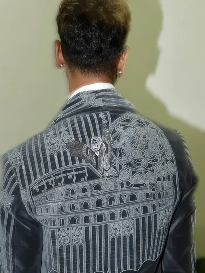 The back of Sarang's grey velvet tuxedo, revealing a striking embroidered narrative of celestial figures and architectural elements. This is wearable art with a deep philosophical undertone.