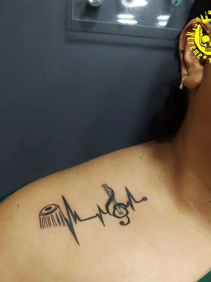 A music lover's tattoo, combining a tabla and a guitar into a heartbeat line. This creative design on the collarbone shows what's truly in their heart.