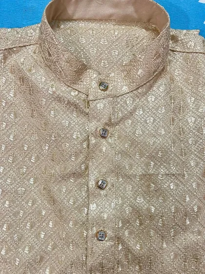 A close-up of a folded beige kurta, showcasing the texture of the self-embroidered fabric and the neat construction of the collar and placket. This is a classic color suitable for both day and night events.