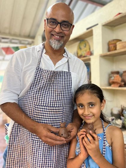 A father and daughter proudly holding the small clay figures they made together. These workshops are all about the shared experience of making something with your own hands.