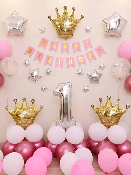 A princess-themed first birthday decoration. This simple setup features pink, white, and metallic balloons, a "Happy Birthday" banner, and large crown foil balloons.