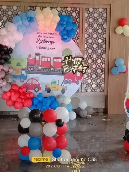 A train and car themed 2nd birthday party. This decoration features a custom backdrop with a train, a balloon arch, and a car-themed cutout.