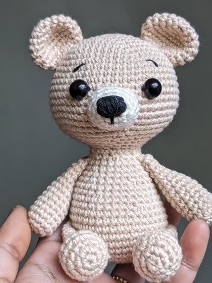 A classic, simple teddy bear in a lovely beige color, small enough to sit in the palm of your hand.
