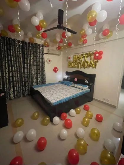 Even a simple decoration can make a big impact. This budget-friendly birthday setup includes red, white, and gold balloons on the ceiling and floor, with 'HAPPY BIRTHDAY' foil letters above the bed to create a festive mood.