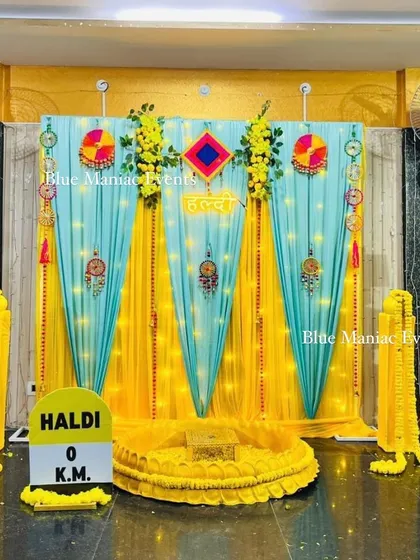 A fun Haldi setup with a blue and yellow theme, featuring traditional hangings and a 'Haldi 0 KM' milestone prop.