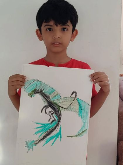 Divyang, a 2nd standard student, proudly shows his dinosaur drawing. He used oil pastels to create this powerful and imaginative creature.