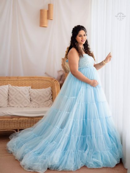 A dreamy portrait of a mom-to-be in a light blue gown, looking radiant by the window in our bright and airy studio.