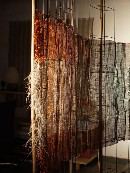 A detail of a woven sculpture from 'Cu+Fibers', showing the transition between different fibers and weaving techniques. The frayed edges and loose threads are an intentional part of the design.