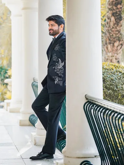 A stylish portrait of the groom leaning against a pillar. This candid-style shot captures his relaxed yet sophisticated look for the reception.