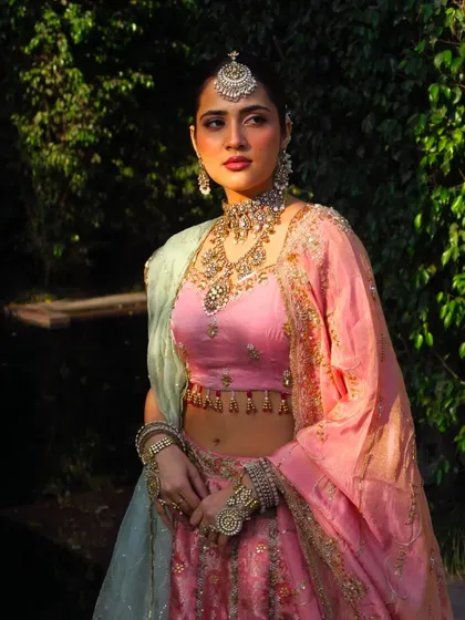 A dramatic portrait in a pastel lehenga. The styling focuses on the contrast between the soft colors of the outfit and the bold, traditional jewelry.