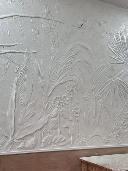 A side-angle view of the completed white tropical relief mural. This perspective emphasizes the three-dimensional quality of the leaves and flowers, which appear to grow right out of the wall.