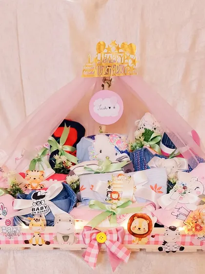 This stunning baby hamper was created for a little one's first birthday. It's a trousseau filled with adorable outfits and toys, all presented in a beautifully decorated animal-themed crate.