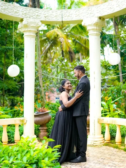 A classic romantic pose in a beautiful garden gazebo. The couple is dressed in matching black formal wear, creating a sophisticated and elegant look.