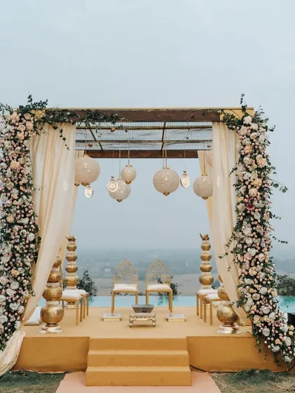 A poolside mandap with a view. The elegant floral pillars and hanging lanterns create a serene and beautiful atmosphere for an evening ceremony.