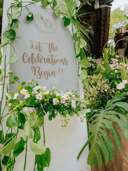 A welcome sign surrounded by lush green foliage and delicate white and pink flowers.