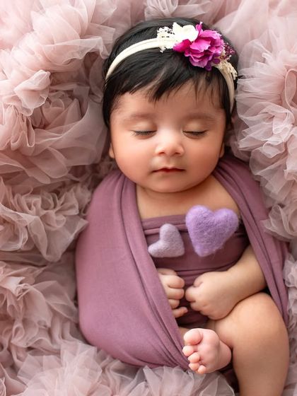 A sweet sleeping portrait with little felt hearts on her chest. The soft purple tones and ruffled fabric create a dreamy and gentle mood.