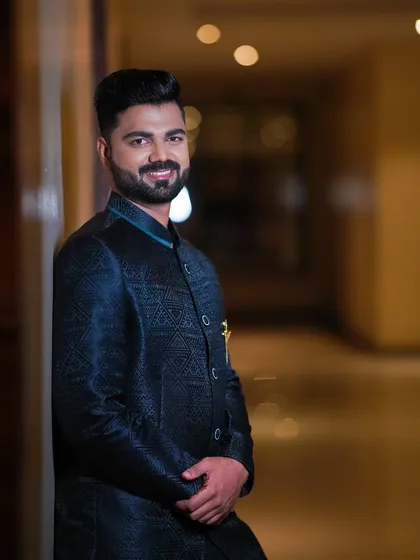 A confident portrait of the groom. The lighting highlights the subtle texture of his jacket and his flawless makeup.