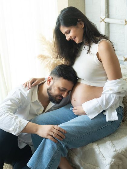 A peaceful moment together. The dad-to-be rests his head on the baby bump, a gesture of love and protection, while the mom-to-be looks on with a gentle smile.
