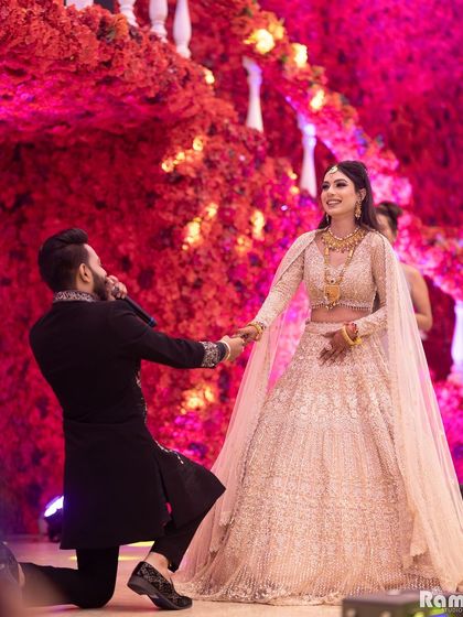 A grand proposal during an engagement ceremony. The groom on one knee against a stunning backdrop of red flowers creates a truly unforgettable and romantic photograph.