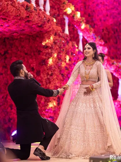 A grand proposal during an engagement ceremony. The groom on one knee against a stunning backdrop of red flowers creates a truly unforgettable and romantic photograph.