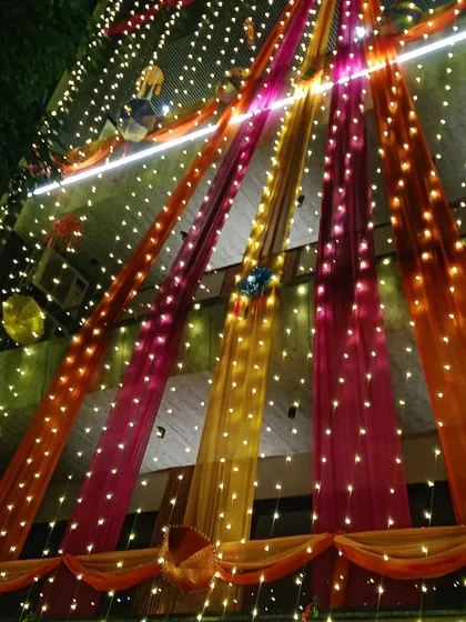 I make sure your house glows at night, creating that perfect 'shaadi ka ghar' feeling. This full building decoration uses colorful drapes and thousands of fairy lights to create a magical welcome for your guests.