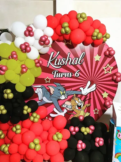 A nostalgic Tom & Jerry theme for a 6th birthday. This decoration features a custom circular backdrop with the iconic duo, surrounded by a balloon arrangement in red, yellow, and black.