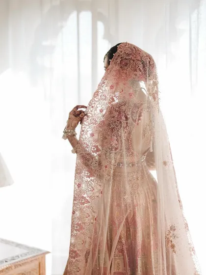 A bride veiled in elegance. This shot, taken against soft window light, highlights the delicate embroidery of her Tarun Tahiliani veil and lehenga, creating a dreamy, almost painterly bridal portrait.