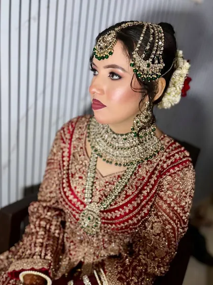 A side view highlighting the intricate hairstyle with a floral bun and the perfectly placed passa and maang tikka. The makeup is flawless from every angle.