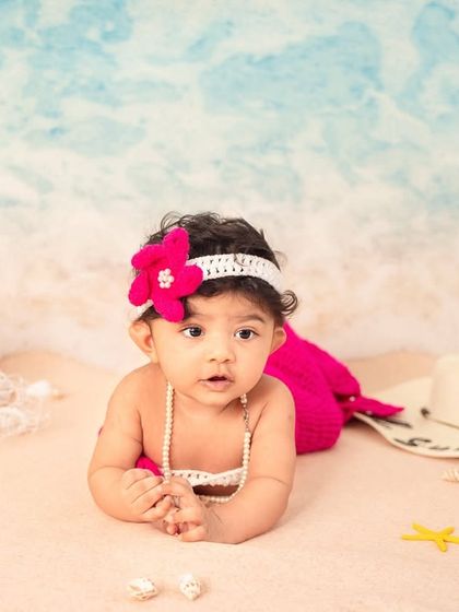 A little mermaid resting on the sand. The pink mermaid tail and seashell details create a whimsical and adorable beach portrait.