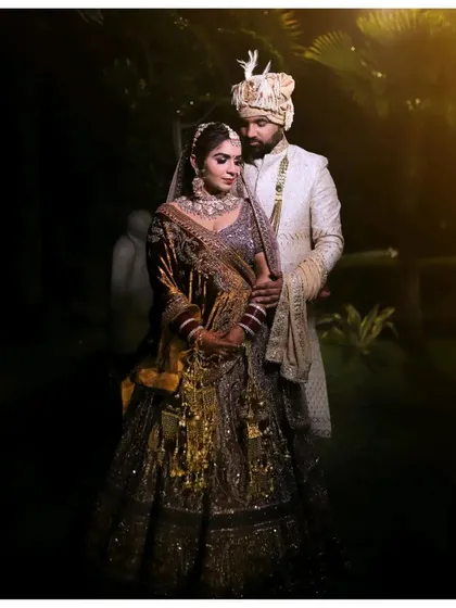 A stunning night portrait of the wedding couple. The dramatic lighting highlights the intricate details of the bride's lehenga and the groom's sherwani, creating a royal and elegant look.