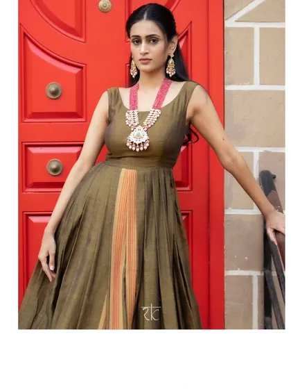 This caramel brown dress with a traditional silk border is a study in understated elegance. It is paired with a vibrant orange hand-embroidered jacket.
