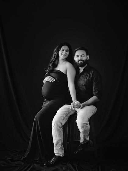 A beautiful seated portrait of a couple in black and white, holding hands and smiling for the camera. A timeless keepsake.