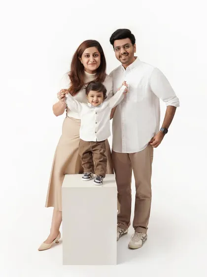 A full-length family studio portrait with the parents standing on either side of their young son, who is proudly standing on a white block.