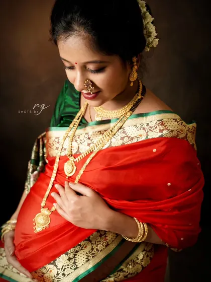 A beautiful close-up of the mom-to-be in her stunning red and green saree, adorned with traditional Maharashtrian jewelry like the nath (nose ring) and gold necklaces.