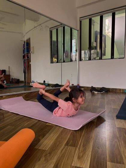 This little girl is mastering Dhanurasana, or bow pose, in our studio. The mirrors help students see their own alignment and progress, building body awareness.