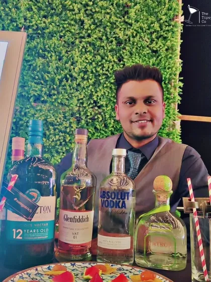 One of our smiling bartenders standing behind a display of premium spirits. We believe a friendly face is just as important as a great drink.