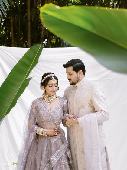 A serene portrait of the couple, framed by a large banana leaf against a clean white backdrop. A modern, artistic take on the classic wedding portrait.