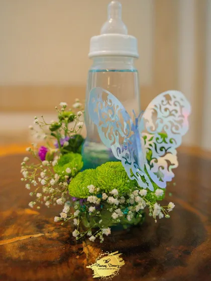 A simple yet creative centerpiece idea for a baby shower. I used a baby feeding bottle as a vase, surrounding it with fresh baby's breath and green chrysanthemums, and finished it with a delicate butterfly cutout for a touch of whimsy.