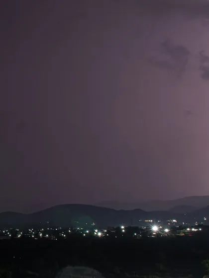 A lightning bolt is captured on the far right of the frame, with the city lights of Pune glowing in the distance.