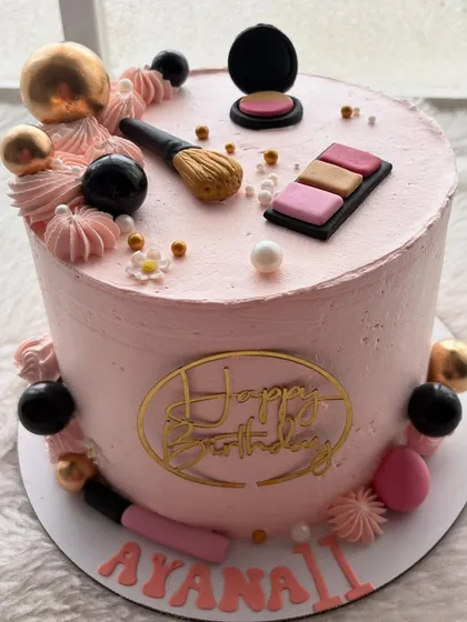 A chic makeup-themed cake for a beauty lover. This pink cake is decorated with handcrafted, edible makeup items like an eyeshadow palette, lipstick, and brushes.