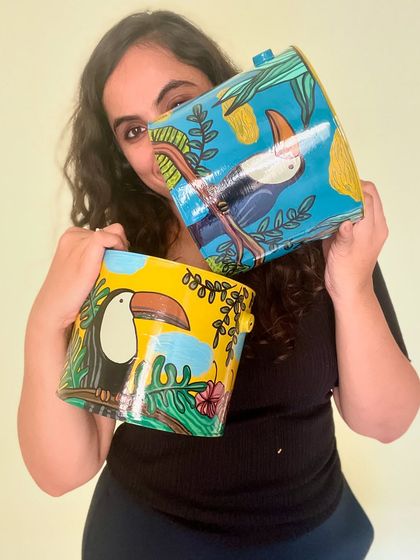 Holding up two of our toucan-themed upcycled tin can planters. Each one is painted with a slightly different background color, making them a unique pair.