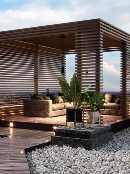 A luxurious rooftop lounge built within a custom wooden slat pergola. This design provides privacy and shade while maintaining an open, airy feel, perfect for creating an elegant outdoor seating area with integrated floor and pendant lighting.